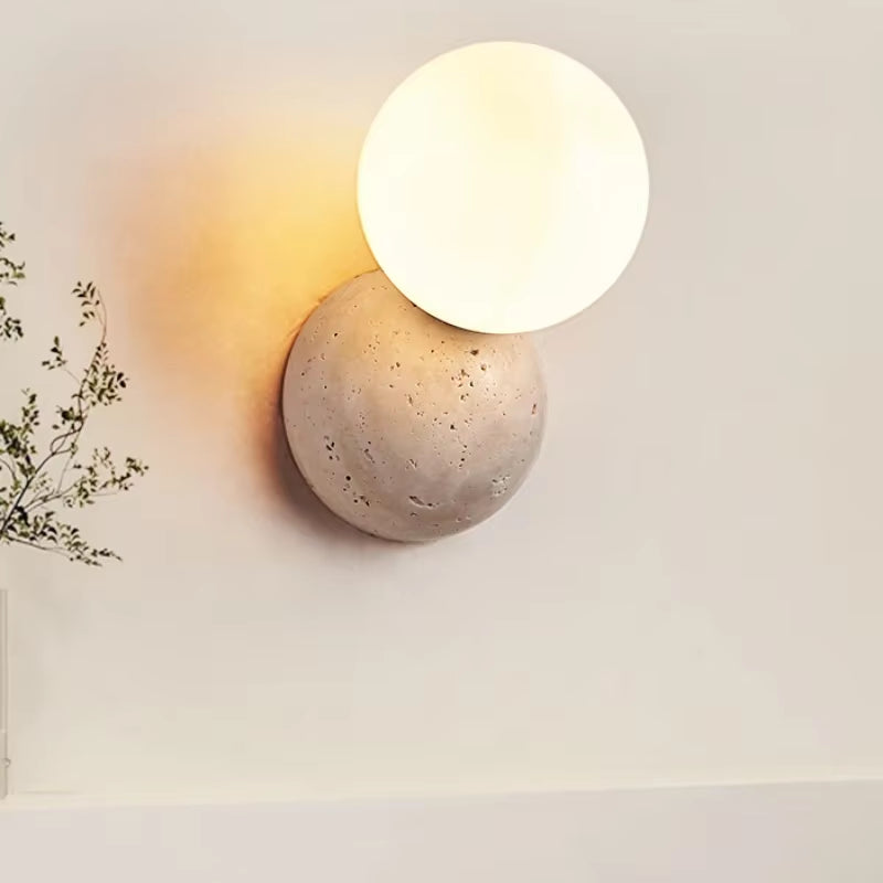 Wall sconce with a frosted glass globe above a stone dome, lit, on a pale wall.