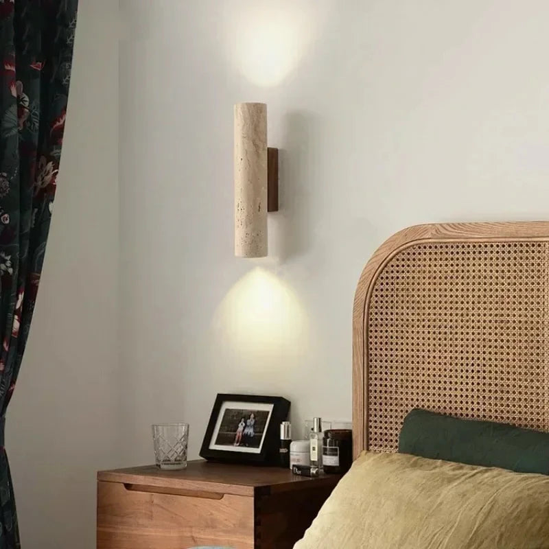Travertine cylinder wall sconce on a walnut bracket beside a rattan headboard.