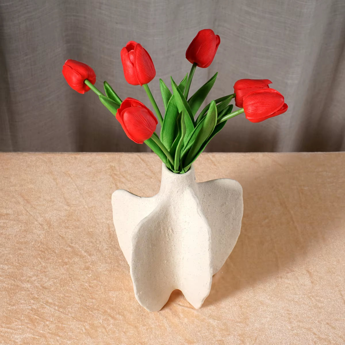 White cleft block ceramic vase with red tulips, seen from a low angle.