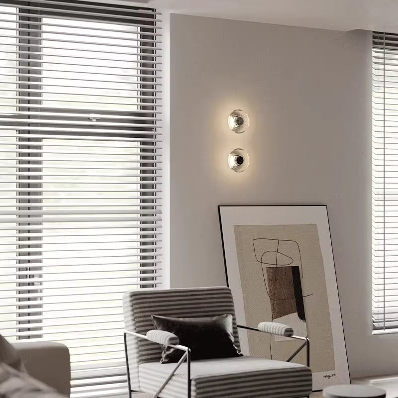 Two clear crystal disc wall sconces, lit, one above the other on a living room wall.