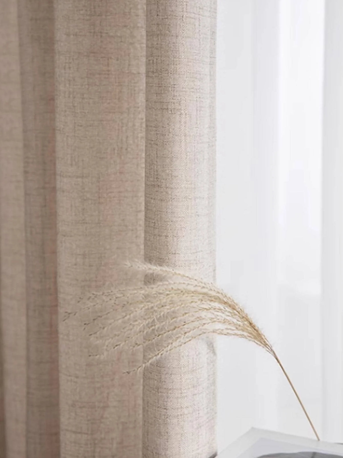 Natural beige textured curtain panel in soft daylight with a dried grass stem in front.