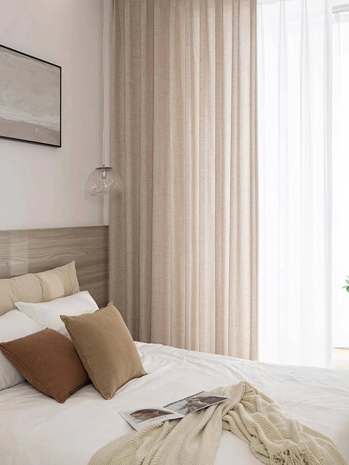 Natural beige semi-sheer curtain panel hanging beside a bed with neutral bedding.
