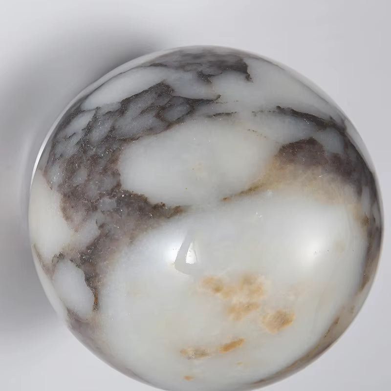 Close view of the marble sphere wall sconce, unlit, showing the gray veining in the white stone.