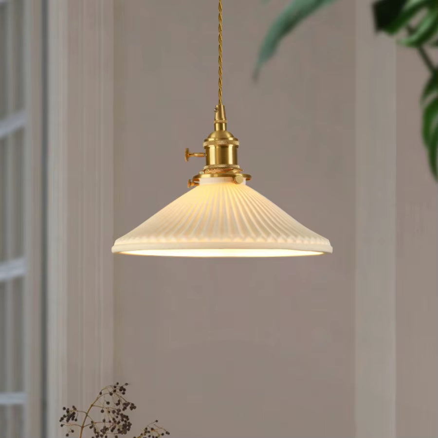 White pleated pendant light with a copper-finish holder, lit, hanging in front of a pale wall.