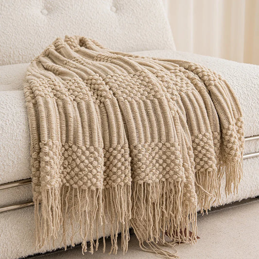 Khaki chunky knit throw with tassels draped over a cream sofa.